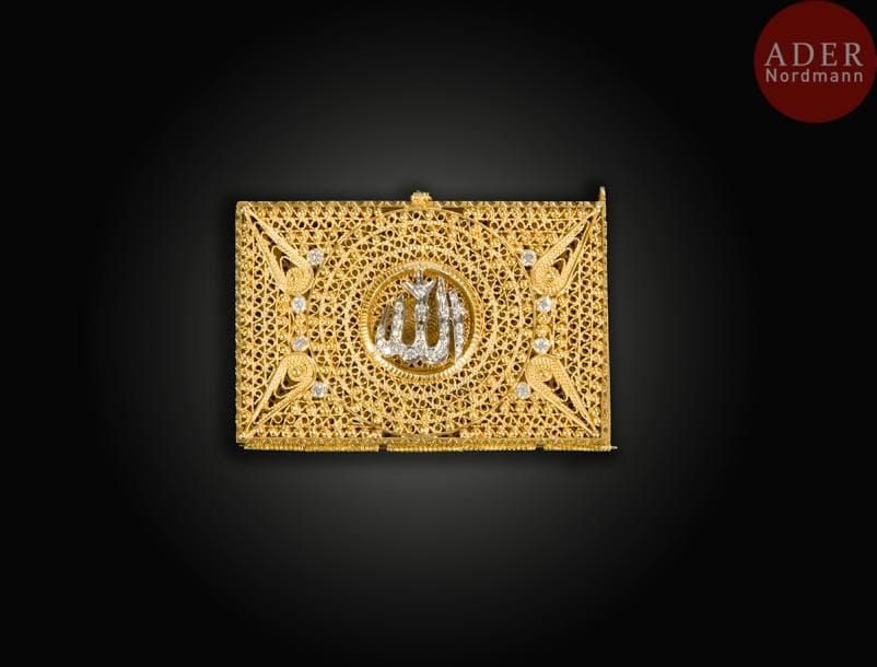 Petite boîte porte-Coran en or, sertie de diamants, Europe ou Proche-Orient, première moitié du XXe siècle
Boîte rectangulaire à charnière, à décor filigrané, sertie de diamants formant le mot Allah au centre. 
Dim. : 6,3 x 4,2 x 1,1 cm
P. : 67 g
A small golden Qur’an box, set with diamonds, Europe or Near East, first half of 20th century.
