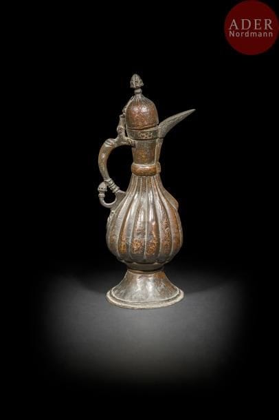 Aiguière en cuivre à patine noire, Inde du nord, XIXe siècle
Panse piriforme godronnée sur large piédouche et large bec verseur. Décor ciselé d’arabesques sur l’ensemble. Anse torsadée achevée d’une tête de dragon et d’un bouton de lotus.
Haut. : 35 cm. 
État : petits enfoncements.
A copper ewer with black patina, North India, 19th century.