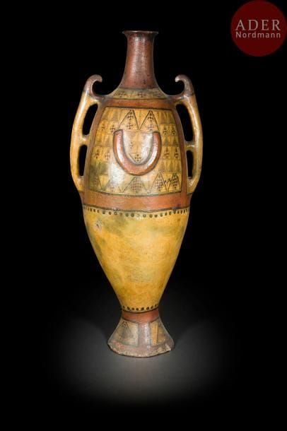 Grande jarre à pied berbère, Grande Kabylie, tribu Aït Daoula, fin XIXe siècle
Terre cuite piriforme à deux grandes anses, sur piédouche, à décor peint en noir, rouge brique sur fond crème orné de motifs géométriques en registre à l’épaulement ; sur la panse, deux panneaux de motifs triangulaires coupés par demi-lunes en relief, en réserve sur fond rouge brique. 
Haut. : 112,5 cm
État : restauration au col.
A large two handeled Berber jar, Great Kabylia, Aït Daoula, late 19th century. 
