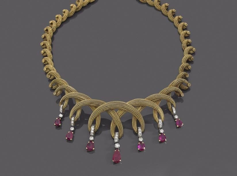 Collier en fils d’or 18K (750 ‰) formant des torsades en chute, le décolleté agrémenté de 7 rubis poires de taille croissante montés chacun en pampille agrémentée de diamants. Travail des années 1960. 
Longueur : 40 cm environ.
Poids brut : 98,5 g (égrisures, givres affleurants). 
Un rubis accompagné d’un pré-rapport  GEM Paris attestant selon son opinion : provenance Myanmar, non chauffé.