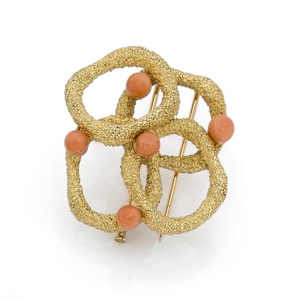 Broche-clip en or 18K (750 ‰) « sauvage » formant quatre anneaux irréguliers, piqué de cabochons de corail. Travail français des années 1960. 
Hauteur : 4,5 cm environ.
Poids brut : 35 g