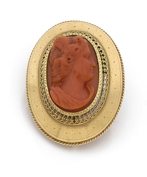 Camée en corail sculpté d’une jeune femme de profil monté en or 18K (750 ‰). Travail français régional antérieur à 1919. Hauteur : 4,2 cm environ.
Poids brut : 10,6 g. 
On joint une paire de pampilles en goutte de corail et un petit fermoir.