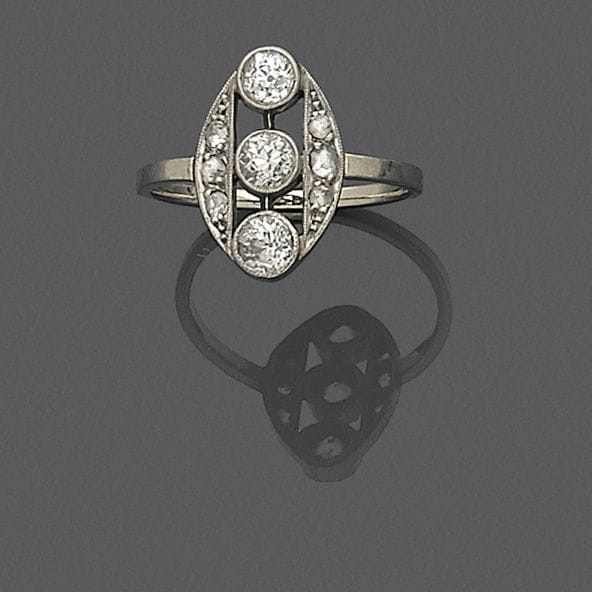 Bague en or gris 18K (750 ‰), le chaton ovale, ajouré, orné de trois diamants de taille ancienne épaulés de diamants taillés en roses. 
Tour de doigt : 54.
Poids brut : 3,1 g (égrisures)