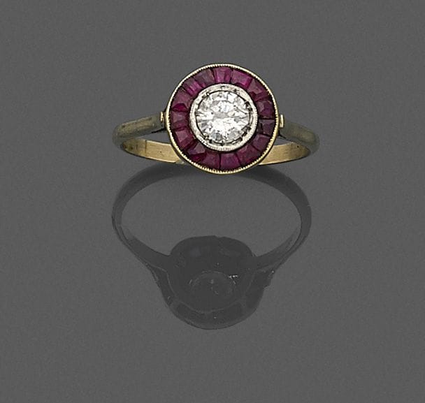 Bague en or 18K (750 ‰), ornée d’un diamant entouré de pierres rouges et de rubis calibrés. 
Tour de doigt : 55.
Poids brut : 2,6 g