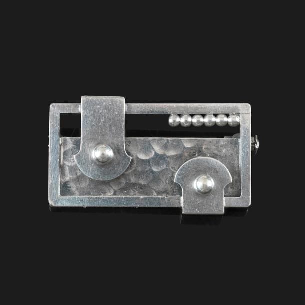 Jean DESPRÉS (1889-1980)

Intéressante broche moderniste en argent.
La platine rectangulaire présente un cadre recevant, en partie, un fond martelé et accueille, en motifs décoratifs, deux agrafes stylisées et un rang perlé. 
Signée J. DESPRÉS à la pointe et porte les poinçons de Maître Orfèvre et de garantie au revers.
Poids : 15 g

Provenance :
Ancienne collection Mme J. (Avallon – France), œuvre acquise par cette dernière directement auprès de l’artiste.