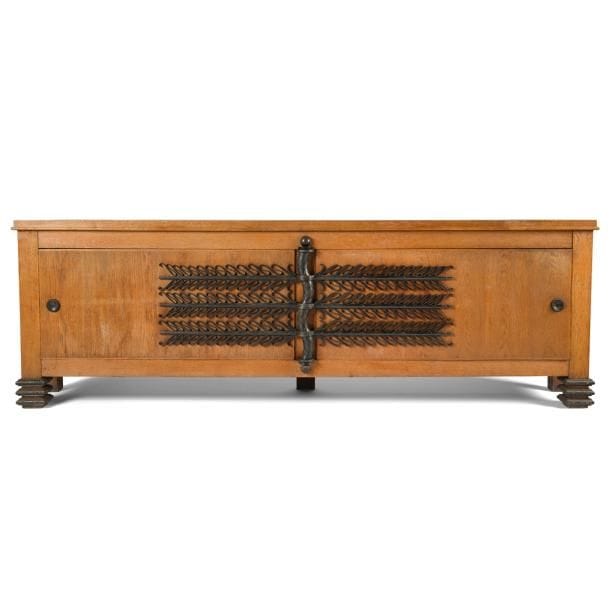 Maurice JALLOT (1900-1971) Décorateur et Raymond SUBES (1891-1970) Ferronnier d’art

Bahut pour une galerie, circa 1942 / 45, possiblement pièce unique
Exceptionnel meuble en chêne et placage de chêne très légèrement sablés.
Le corps quadrangulaire repose sur des pieds d’angle et présente un plateau à la moulure en léger débordement.
La façade s’ouvre par deux longues portes à charnière centrale.
Les pentures, l’important gond central, les prises et les bagues de réception de pied en fer forgé patiné et aux décors en creux.
Les parties latérales en panneaux décaissés.
État d’usage.
86 x 264 x 48 cm

Provenance :
- Collection Delattre. Œuvre acquise directement auprès de l’artiste.
- Par descendance

Bibliographie :
- Décors - Album édité par le rayonnement français, Paris, 1945. Notre meuble reproduit page 21.
- Mobilier et Décoration - N° 4 d’avril 1948. Notre meuble reproduit page 47 avec la mention du nom de M. Delattre collectionneur.
- La Maison française – N° 22 de novembre 1948. Notre meuble reproduit page 27.
- Ensembles mobiliers, volume 5 - Éditions Charles Moreau, Paris, c. 1948. Un meuble identique ou notre meuble reproduit planche 7.
- Meubles nouveaux - Présentation de Guillaume Janneau, éditions Charles Moreau, Paris, c. 1948. Notre meuble reproduit planche 22.