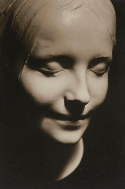 Albert Rudomine (1892-1975)

Inconnue de la Seine, 1927. 

Épreuve argentique d’époque sur papier mat. Mention "Les Images de Rudomine" tapuscrite au verso.

14,5 x 10,5 cm 

La légende autour de ce portrait mortuaire d'une jeune femme souriante, inconnue et probablement décédée dans les années 1880, fascine et alimente la littérature et les arts du début du siècle. Les copies du célèbre moulage ornent les intérieurs d'artistes qui spéculent sur la vie de la défunte et les causes de son supposé suicide par noyade. "Dans les cordes se mourant à l'infini J'entends la voix de ta beauté. Dans les foules blêmes des jeunes noyées Tu es plus blême et ensorcelante que toutes. Au moins dans les sons reste avec moi! Ton sort fut avare en bonheur, Alors réponds d'un posthume sourire moqueur De tes lèvres de gypse enchantées. Paupières immobiles et bombées, Cils collés en épaisseur. Réponds! À jamais, à jamais, vraiment? Mais comme tu savais regarder" Vladimir Nabokov, L'Inconnue de la Seine, 1934.