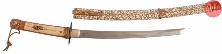 JAPON
Shinto wakizashi, shinogi zukuri, trempe effacée, nakago percé d’un mekugi ana. Nagasa 38 cm. Signé Sadayoshi. (Accidents).
Tsuba moko gata en fer à décor de lettré regardant la lune, menuki figurant des dragons autour de ken, saya à l’imitation du galuchat blanc. (Monture dépatinée, accidents au saya).