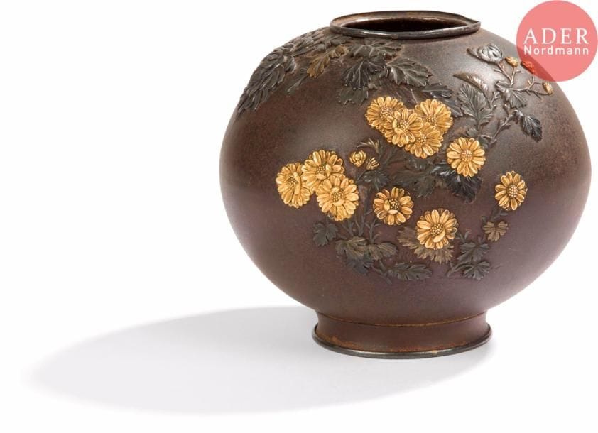 JAPON - Époque MEIJI (1868 - 1912)
Petit pot arrondi en bronze à patine brune à décor en relief en shibuichi et cuivre doré de branches de fleurs de chrysanthèmes épanouies. (Légèrement tordu en bordure de col). Dessous du pied en shibuichi.
H. : 9,1 cm.