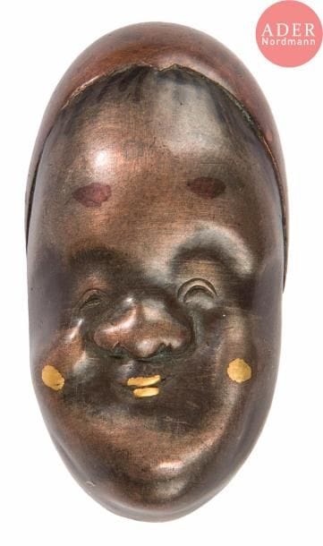 JAPON - Époque MEIJI (1868 - 1912)
Tête d’Okame formant boucle en shibuichi les yeux rieurs.
H. : 4 cm. 