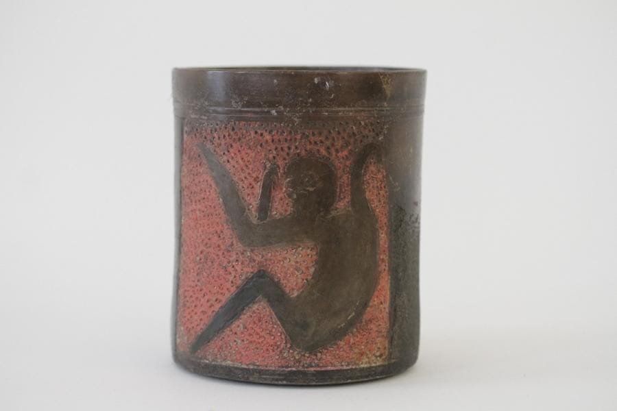 Vase cylindre orné d'un singe qui se détache sur le fond rouge d'un cartouche.  Chez les mayas, le singe représente le dieu des arts. Terre cuite brune à engobe brun noir avec cinabre. Traces d'oxyde de manganèse et de racines. Culture Maya, Mexique, 600-900 apr. J.-C.  H. 13 - Diam. 11 cm Provenance: Collection Ulrich Hoffmann, organisateur et auteur d'expositions et d'ouvrages sur l'art précolombien, Stuggart, Allemagne. Bibliographie: Exposé durant 10 ans au Ceramik Museum de Dusseldorf, Allemagne. Venet M. F. Robert, Drouot, le 15/06/2013, lot.57