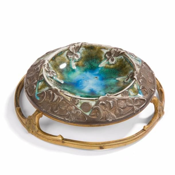 Paul LOUCHET (1854-1936)
Trèfle
Cendrier. Épreuve en porcelaine émaillée façon flammé. Pourtour et armature en laiton et bronze patinés argent et or. Un éclat et légères fissures dans l’émail au centre. Porte le cachet circulaire Paris LOUCHET Ciseleur. D. 15 cm 
