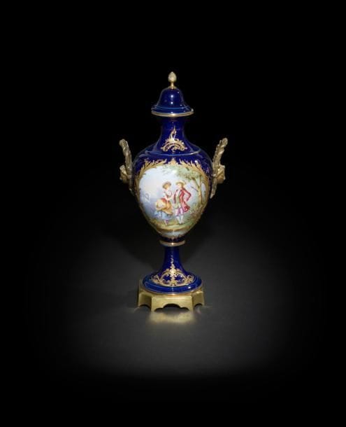 Sèvres (genre de)
Vase couvert de forme balustre en porcelaine et bronze doré à décor polychrome d’un couple galant et d’un paysage dans deux réserves sur fond bleu, la base et les anses en bronze doré.
Fin du XIXe siècle. 
H. 44 cm
Petit éclat sur le bord du couvercle et quelques usures d’or