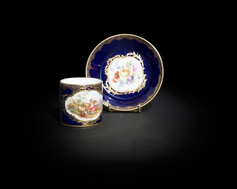 Meissen
Tasse et sa soucoupe en porcelaine à décor polychrome d’une bergère et brebis dans un paysage et d’un bouquet de fleurs dans des réserves cernées de rinceaux rocaille or sur fond bleu.
Marquées : épées croisées en bleu.
XIXe siècle. 
H. 6,5 cm, D. 13 cm
