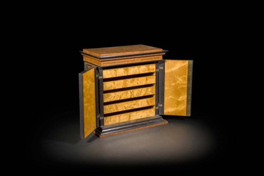 Cave à cigares en bois de loupe et bois noirci, à pilastres et corniche saillante, ouvrant à deux vantaux découvrant cinq tiroirs.
Fin du XIXe siècle (petits manques)
H : 40 cm, L : 40 cm, P : 24