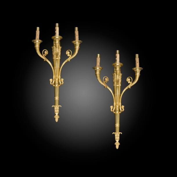 Paire d’appliques à trois lumières en enroulement et fût à brandon.
Style Empire, fin du XIXe siècle
H : 42 cm

Plusieurs appliques d’un modèle similaire ont été livrées en 1810 par la maison Thomire-Duterme pour le Grand Trianon et le Château de Fontainebleau.