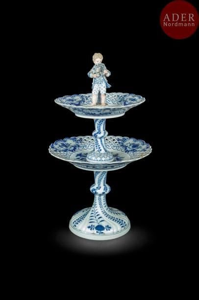 Meissen
étagère en porcelaine à deux plateaux à décor en camaïeu bleu à l’oignon, les bords ajourés, elle est surmonté d’une figure de jeune garçon tenant une couronne de fleurs.
Marquée : épées croisées en bleu.
Fin du XIXe siècle. 
H. 42 cm
Accidents sur le bord