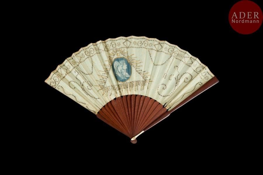 Louis XVI, Marie-Antoinette et Louis XVII, vers 1790-1800
Éventail plié, la feuille double en soie crème décorée au centre d’une gravure présentant les profils du roi de France, de la reine et du dauphin. Elle est insérée dans un triangle maçonnique surmonté d’un ovale (l’œil de la Providence ?).
Monture en bois, la tête rehaussée d’une petite plaque en os.
H.t. 27,9 cm/ H.f. 15,2 cm (coupures de la feuille et usures)