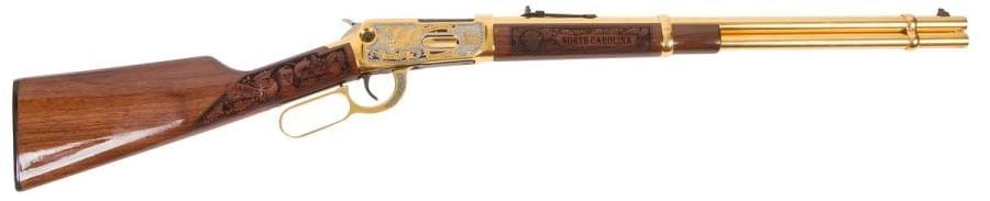 Carabine Winchester modèle 94AE « Mecklenburg County 1 of 10 », calibre 45 Colt. 
Canon doré et gravé de 49 cm (20’’). Finition dorée, argentée et gravée (SBR Etchings). Crosse en noyer sculpté de feuilles de chêne, têtes de bison et de d’homme, diligence. 
Longueur totale : 96 cm 
Catégorie C à déclarer. 
N°IA01415. N° 5 sur 10. 