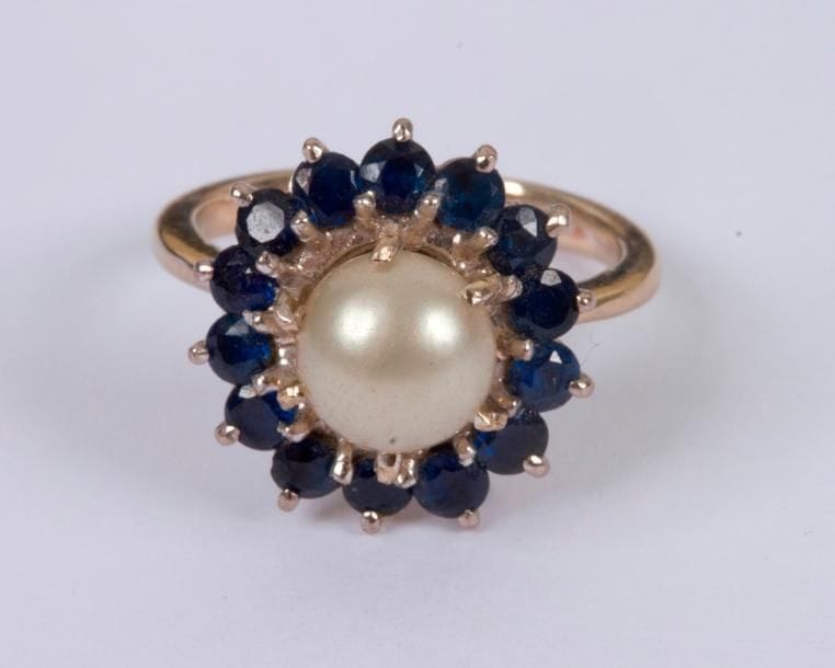 Bague en or gris 18K (750 ‰), ornée d'une perle bouton fantaisie entourée de pierres bleues. Tour de doigt : 48. Poids brut : 5,2 g