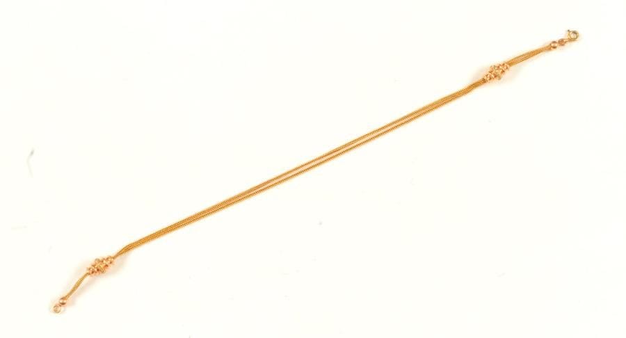 Chaîne de montre à deux brins en or 18K (750 ‰), maillons colonne, ponctuée de deux motifs coulissants en 2 tons d'or. Travail français de la fin du XIXe siècle. Longueur : 31 cm environ. 
Poids : 12,5 g 