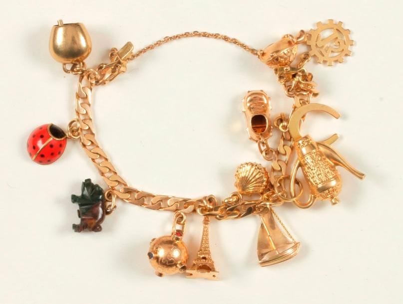 Bracelet en or 18K (750 ‰), maillons gourmette, retenant en pampilles, 12 breloques en or : une clochette, une coccinelle émaillée, un cochon en pierre dure, une sphère piquée de pâtes de verre, une Tour Eiffel, une coquille Saint-Jacques recélant une perle, une théière, un voilier, un soulier, un fer à cheval, une tortue, le chiffre 13. 
Poids brut : 30,9 g