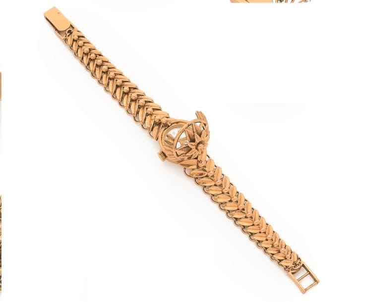 Montre de dame à cachette en or 18K (750 ‰), cadran rond ajouré d’une fleur, bracelet en or 18K articulé de feuilles stylisées. Travail français des années 1950. Longueur : 17,5 cm environ. 
Poids brut : 46,3 g