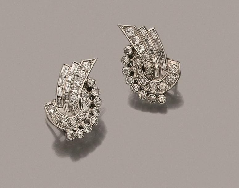 Paire de motifs d’oreilles en platine et or gris 18K (750 ‰) formant des courbes et des rubans sertis de diamants ronds et calibrés. Travail français des années 1930. Hauteur : 2,5 cm environ. 
Poids brut : 13,8 g (égrisures)