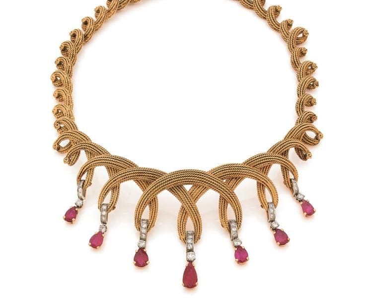 Collier en fils d’or 18K (750 ‰) formant des torsades en chute, le décolleté agrémenté de 7 rubis poires de taille croissante montés chacun en pampille agrémentée de diamants. Travail des années 1960. 
Longueur : 40 cm environ.
Poids brut : 98,5 g (égrisures, givres affleurants). 
Un rubis accompagné d’un pré-rapport GEM Paris attestant selon son opinion : provenance Myanmar, non chauffé.