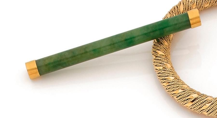 Broche en or 18K (750 ‰), ornée d’un jade tubulaire. Travail extrême-oriental des années 1920. Longueur : 8,5 cm environ. 
Poids brut : 14,1 g