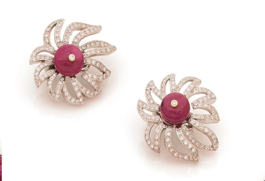 Paire de motifs d’oreilles en platine et or gris 18K (750 ‰) dessinant des fleurs stylisées, les feuilles serties de diamants ronds, le cœur en bille aplatie de rubis piqué d’un petit diamant. Hauteur : 3,5 cm environ. 
Poids brut : 35,1 g