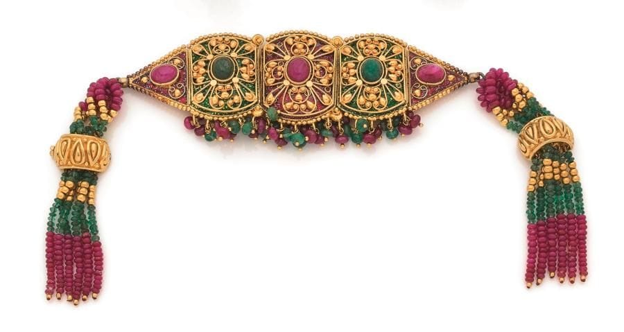 Bracelet en or 18K (750 ‰), articulé de motifs quadrangulaires émaillés appliqué d’arabesques, chacun centré d’une racine d’émeraude ou d’un rubis cabochon, retenant en pampilles des billes d’émeraudes et de rubis, le fermoir en or 18K terminé de pompons de rubis et d’émeraudes. Longueur : 20,5 cm environ. 
Poids brut : 91,2 g (chocs)