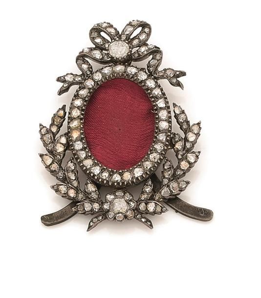 Petit cadre pour photo en argent et en or 18K (750 ‰), surmonté d’un nœud et souligné par une couronne de feuilles, serti de diamants taillés en roses. Travail du début du XXe siècle. Hauteur : 5 cm environ. 
Poids brut : 22 g