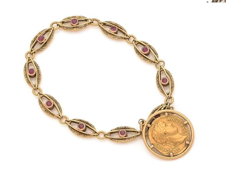 Bracelet en or 18K (750 ‰), articulé de maillons ovales ajourés, chacun serti d’une pierre rouge, retenant en pampille une pièce en or à l’effigie d’Hadrien. 
Poids brut : 27 g