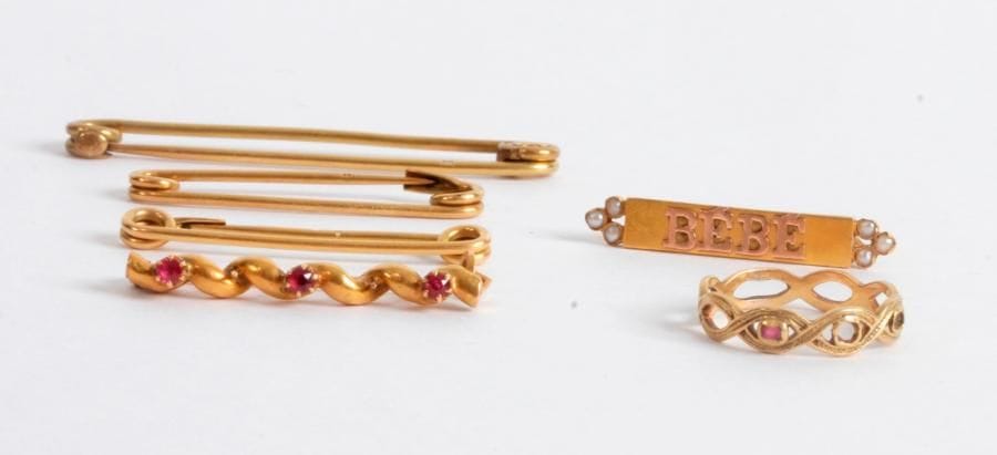 Lot de 3 bijoux en or 18K (750 ‰) comprenant : une bague ajourée d’ovales, une broche portant l’inscription Bébé, une autre broche agrémentée de trois rubis. 
Poids brut : 5 g (on joint 3 épingles de nourrice en métal)