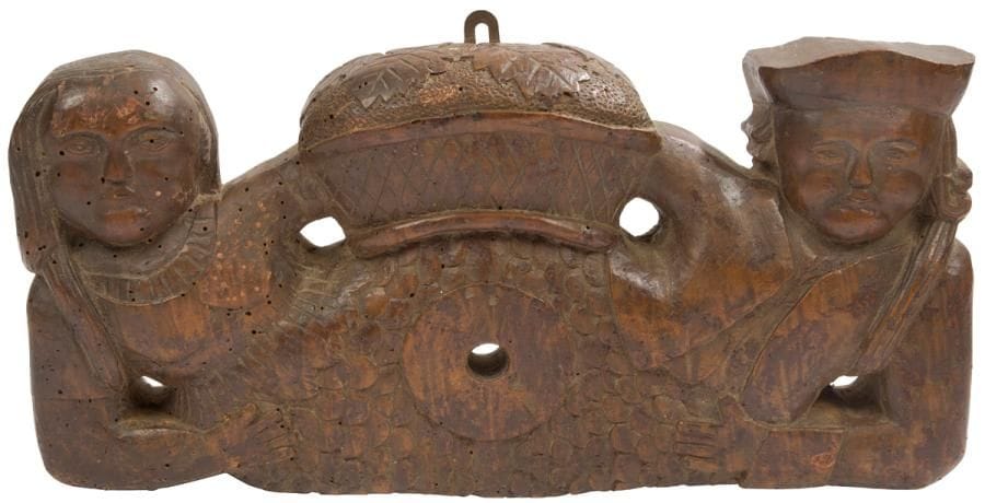 Alsace, XVIIIe siècle
Clé de foudre en noyer sculpté, à décor d’une femme au corps de sirène et d’un homme en coiffe, entourant un panier recouvert de feuilles de vigne. 
Longueur : 43 cm - hauteur 21 cm