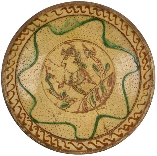 Flandres, XVIIIe siècle
Plat rond en terre cuite émaillée polychrome à décor central d’un fumeur de pipe de profil dessiné a sgraffito entouré d’un décor de frises géométriques.
Fente, restauration ancienne aux agrafes
Diamètre : 36,5 cm