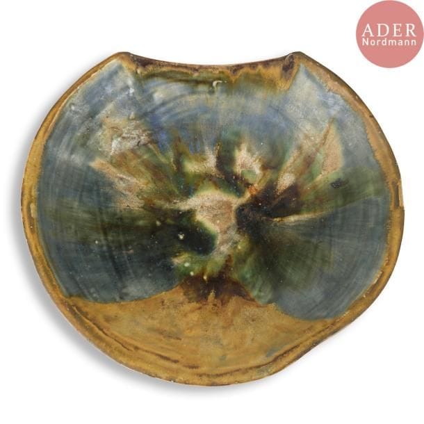 François BOQUEL (1928-2017)
Grand plat circulaire creux, à un bord tronqué. Épreuve en céramique à décor émaillé rayonnant brun, bleu, vert et beige. Monogrammé F.B. et daté 5.(19)84 sous la base. D. 40 cm
Né à Nancy le 15 août 1928, François Boquel quitte l’école et sa famille à 16 ans. 

Né à Nancy le 15 août 1928, François Boquel quitte l’école et sa famille à 16 ans. Fasciné par les arts du feu, c’est en parfait autodidacte qu’il s’installe à Vallauris dans les années 1950. Dans le village, il travaillera notamment à l’Atelier Les Archanges aux côtés de Gilbert Valentin. Il nouera également à cette époque une solide amitié avec le peintre André Cottavoz, avec qui il restera longtemps en contact, le céramiste François Raty, mais aussi Jacques Prévert avec lequel il aimait échanger sur l’art.  Il s’installe en Île-de-France dans les années 1960, région qu’il ne quittera plus jusqu’à son décès à Meudon en 2017. Bien qu’éloigné géographiquement du village aux cent potiers, il ne cessera de pratiquer l’art de la céramique, en témoignent les œuvres présentées ci-après.