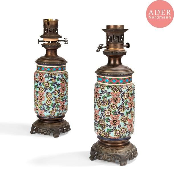 ÉMAUX de LONGWY 
Paire de lampes à pétrole. Épreuves en céramique à décor d'émaux cloisonnés polychromes dans le goût de l'Orient, montures en bronze à décor ajouré. Surmontée chacune d'un fût et d'un globe en verre à décor végétal gravé. Un éclat et petites égrenures aux globes. Chaque corps de lampe en céramique marqué LONGWY en creux sous la base. H. 63 cm
