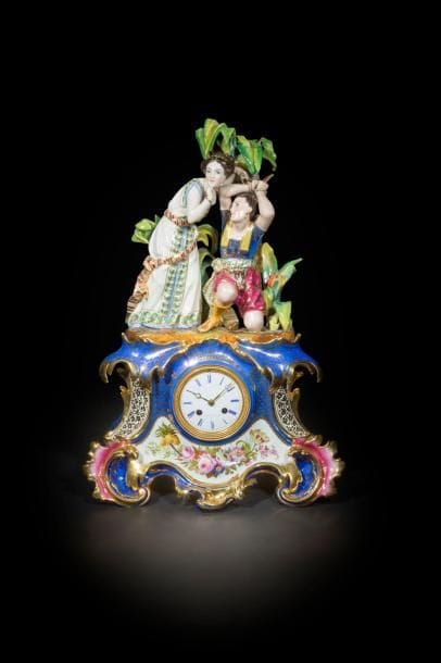 Paris
Pendule en porcelaine formée d’une femme délivrant un homme attaché à un arbre, sur une base rectangulaire de style rocaille à décor polychrome de bouquets de fleurs sur fond bleu et or.
Milieu du XIXe siècle. 
H. : 56 cm
