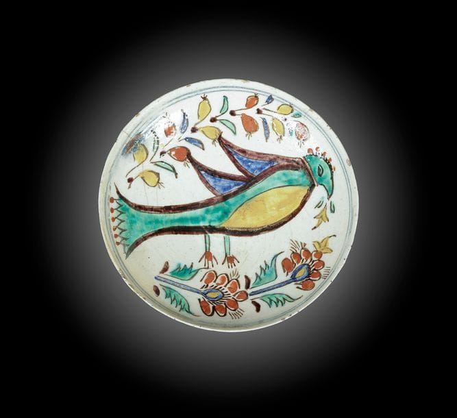 Coupelle à l’oiseau, Turquie ottomane, Kütahya, XVIIIe siècle
Céramique siliceuse peinte à main levée en polychromie sur engobe blanc et sous glaçure transparente. Un oiseau de profil entre deux tiges florales. Deux lignes bleues au bord encerclent le tout.
D. : 14 cm ; H. : 4 cm
État : fracture recollée et petits manques au bord.

A Kutahya pottery dish, Ottoman Turkey, 18th century
