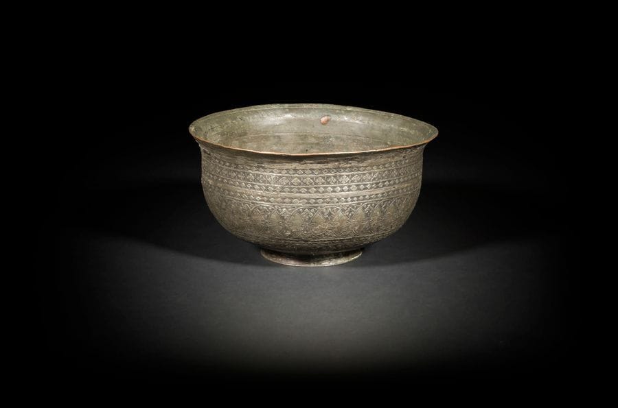 Coupe en cuivre étamé, Iran, XIXe siècle, et grand bassin en laiton, Égypte ou Syrie, probablement XIXe siècle
- Coupe à panse hémisphérique sur piédouche, à décor ciselé de registres de cercles entrelacés et de motifs losangés au col. Gravé à la base « Heydar », probablement le nom du fabricant.
H. : 10,9 cm, D. : 20 cm ; état : petites fentes.
- Bassin à panse tronconique en laiton, à décor ciselé de médaillons calligraphiés en thuluth intercalés de médaillons d’entrelacs de palmettes bifides.
H. : 24 cm, D. : 29 cm ; état : petits enfoncements.

A tinned copper bowl, Iran, 19th century and a large brass basin, Egypt or Syria, 19th century