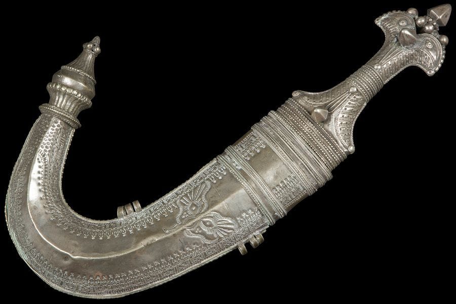Poignard, jambiya, Yemen, XXe siècle
A lame courbe en acier à double tranchant et nervure médiane. Monture et fourreau en métal argenté à décor estampé d’un oiseau aux ailes déployées sur le fourreau et frise de motifs géométriques à forte bouterolle. Manche à cabochons pyramidaux et registres perlés au milieu de motifs striés.
L. : 40 cm

A silvered dagger (jambiya), Yemen, 20th century