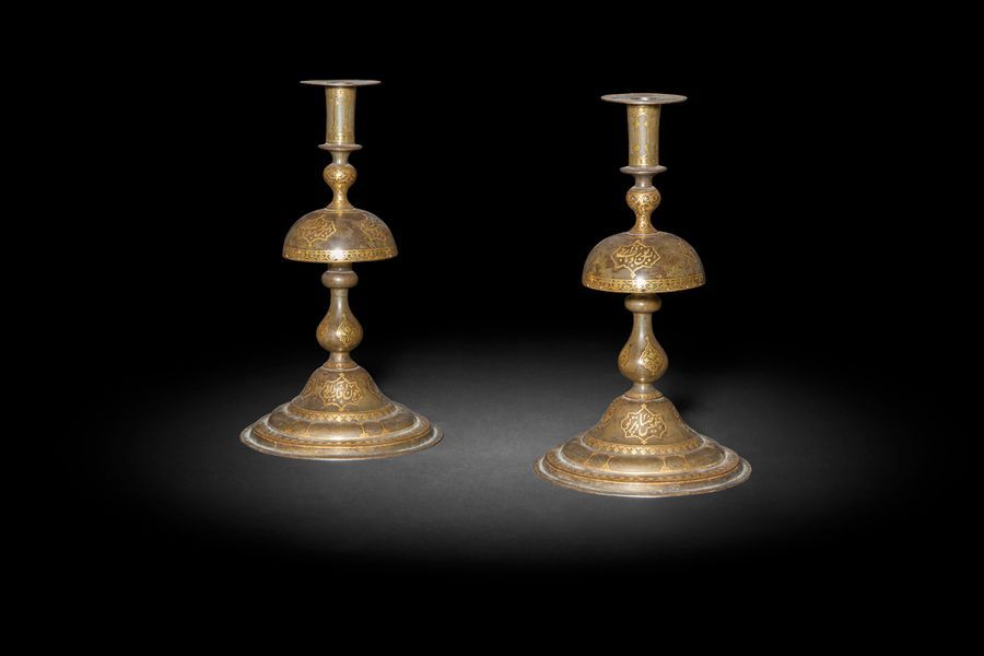 Paire de chandeliers en acier damasquiné d’or, Iran Qajar, XIXe siècle
Chaque chandelier à large bobèche et fût animé d’une coupe inversée reposant sur une base en doucine, orné sur l’ensemble de cartouches inscrits d’une poésie persane magnifiant le chandelier et sa lumière étincelante : « Ce chandelier d’acier est tout étincelant comme l’or pur. Quel chandelier, il brille comme le soleil dans l’assemblée des amis ».
H. : 29,5 cm ; D. base : 17 cm

A Pair of gold-damascened steel candlesticks, Qajar Iran, 19th century