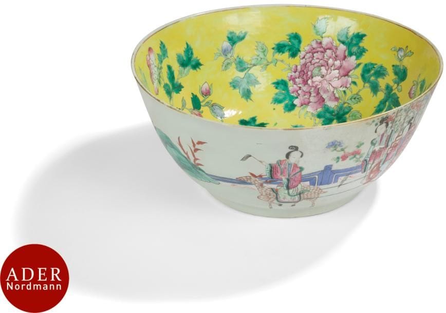 CHINE - Époque TONGZHI (1862 - 1874)
Grand bol en porcelaine émaillée polychrome à décor de dignitaires et jeunes femmes sur une terrasse jouant avec des chimères à l’extérieur, et  l’intérieur de pivoines et bourgeons dans leur feuillage sur fond jaune. 
Diam. : 36,5 cm (restaurations).
