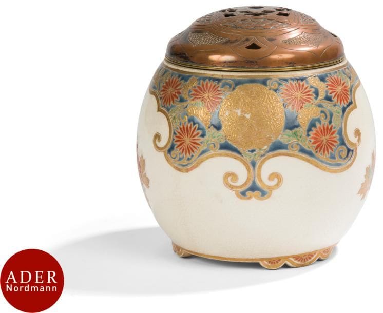 JAPON, Fours de Satsuma - Époque MEIJI (1868 - 1912)
Brûle-parfum tripode en faïence de Satsuma à décor émaillé polychrome et or de fleurs de chrysanthèmes et feuilles d’érables sur fond bleu dans une réserve polylobée le long de l’épaulement, et de fleurs de lotus dans leur feuillage sur la panse. 
H : 9,5 cm. La bordure montée de métal. Le couvercle en laiton ajouré d’un fleuron central.
