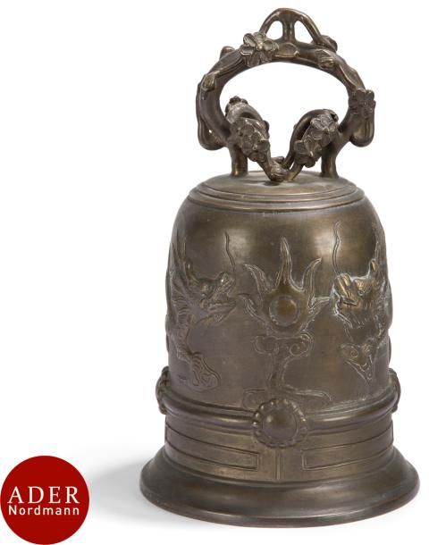 JAPON - XIXe siècle
Cloche en bronze à patine brune à décor en relief sur la panse de dragons à la recherche de la perle enflammée, la prise formant branche de cerisiers en fleur. 
H : 24 cm
