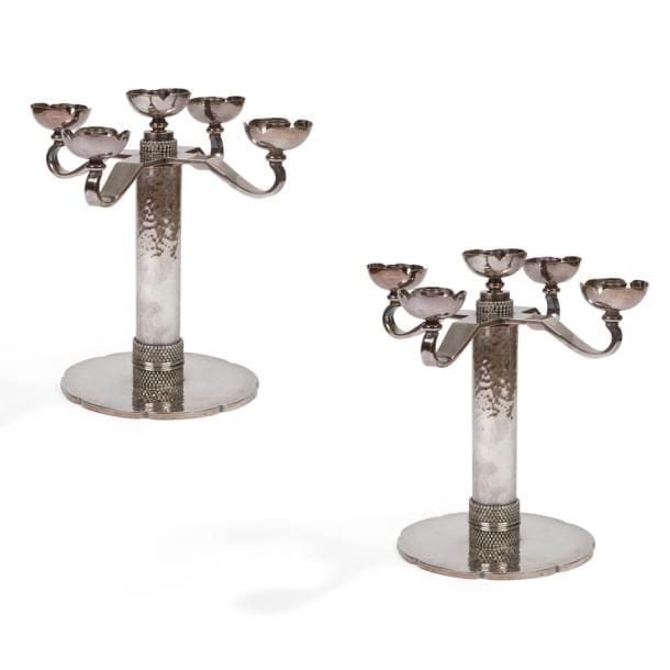 JEAN DESPRÉS (1889-1980)

Rare, élégante et importante paire de candélabres à cinq feux ; quatre bras de lumière et une bobèche centrale. 
Épreuves réalisées en métal argenté.
Les fûts cylindriques et martelés reçoivent, chacun sur leur partie basse, un double motif de cinq rangs perlés séparés par un double jonc.
Les bases, également martelées, présentent un pourtour polylobé.
Les bras de lumière, traités lisses et terminés en croche, et les fûts reçoivent chacun une bobèche quadrilobée ; celles du centre reposant, chacune, sur un cylindre orné d’un quadruple rang perlé.
Chaque candélabre signé J. DESPRÉS à la pointe sous la base et porte le poinçon de Maître Orfèvre sur la tranche de la terrasse.
Hauteur : 30,5 cm

Provenance :
- Madame D., ancienne propriétaire de l’Hôtel de la Poste et du Lion d’Or à Vézelay (Près d’Avallon - France), œuvre acquise directement auprès de l’artiste dans sa boutique d’Avallon.
- Madame P., Vézelay, fille de la précédente.
- Madame N., Chamoux près Vézelay, fille de la précédente et petite-fille de Madame D.
