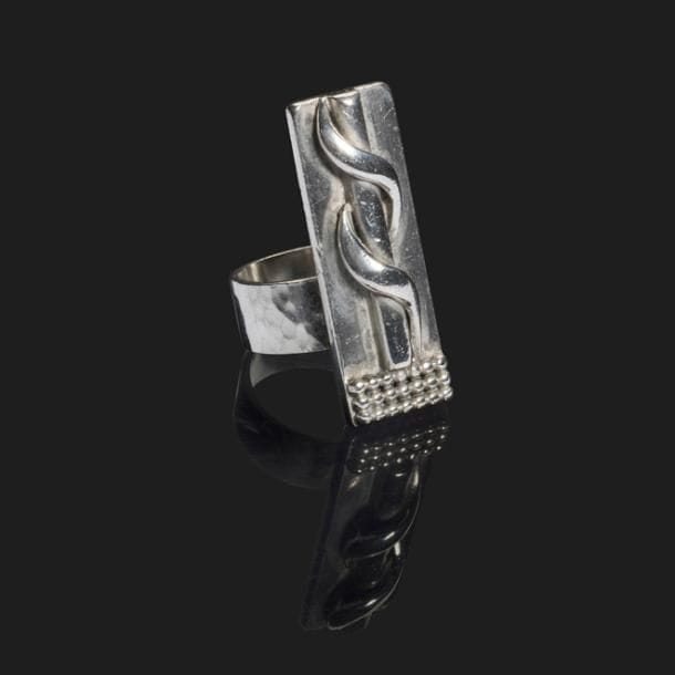 JEAN DESPRÉS (1889-1980)

Rare bague moderniste en argent.
La longue plateforme reçoit, en application, un motif de cylindre enrichi d’un enroulement et un pavement de sphères.
Le large anneau présente une surface martelée.
Signée Jean DESPRÉS à la pointe sous la plateforme et porte les poinçons de Maître Orfèvre et de garantie sur l’anneau.
Poids brut : 21,02 g

Provenance :
Ancienne Collection Madame L., Joux-la-Ville. Œuvre acquise par cette dernière directement auprès de l’artiste. 
