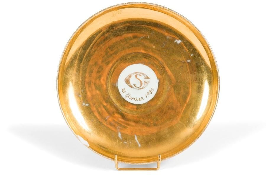 [Sacha GUITRY] Soucoupe en porcelaine blanche et or à décor au centre du monogramme SG et la date 21 février 1936 Marquée au dos Delvaux / rue Royale / Paris Diamètre : 18,5 cm Éclat et usures d’or
